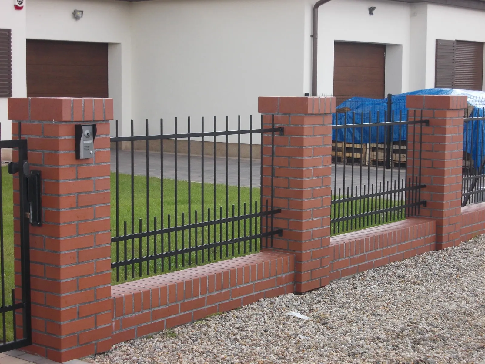 Ogrodzenie z czarnych prętów stalowych między ceglanymi słupkami